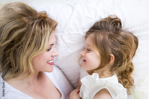 Cute little girl and her mother lying on a bed