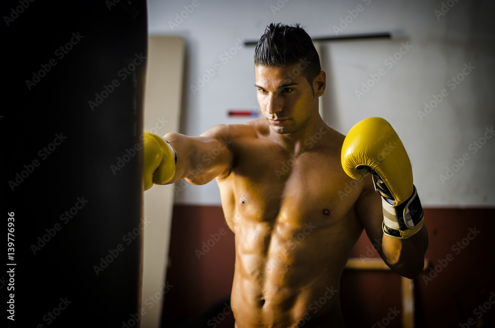 Handsome shirtless and muscular man with boxer's gloves in a gym