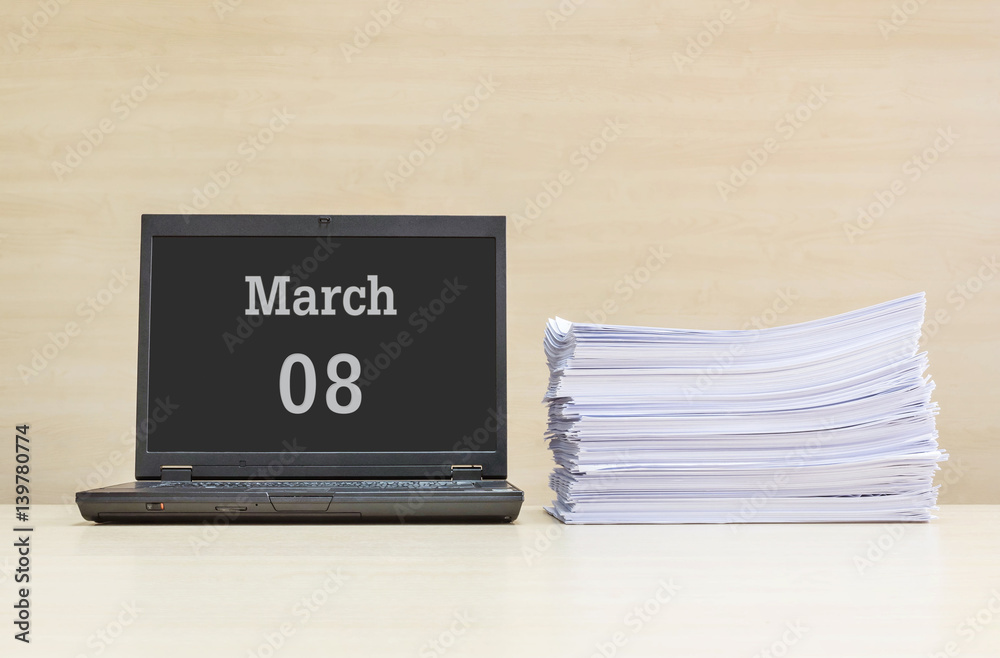 Closeup computer laptop with march 8 word on the center of screen in calendar concept and pile of work paper on wood desk and wood wall in work room textured background with copy space Closeup computer laptop with march 8 word on the center of screen in calendar concept and pile of work paper on wood desk and wood wall in work room textured background with copy space