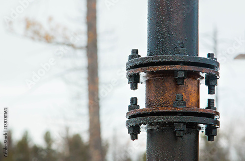 Rusty oily bolted pipe joint covered with crude oil associated gas condensate surge spill on blurred winter forest background