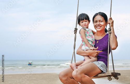 Asian Mum and daughter swinging on the sea coast