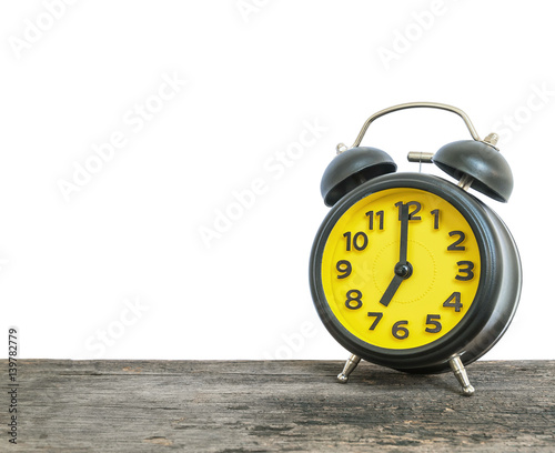 Closeup black and yellow alarm clock for decorate in 7 o'clock on old brown wood desk isolated on white background with copy space