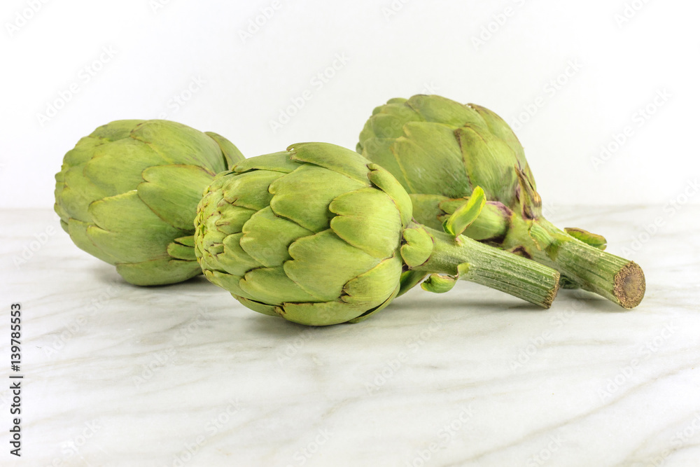 Fototapeta premium Artichokes on white marble texture with copyspace