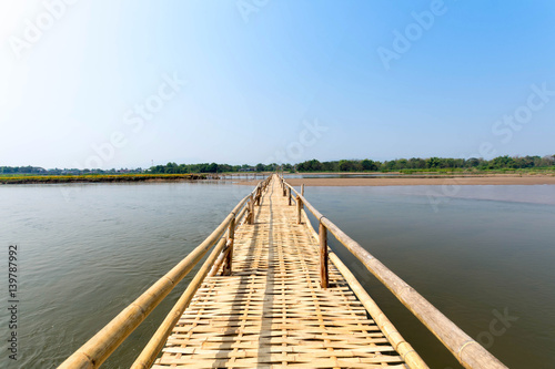 Fototapeta Naklejka Na Ścianę i Meble -  beautiful long bamboo bridge on river with blue sky at sunny day. soft focus