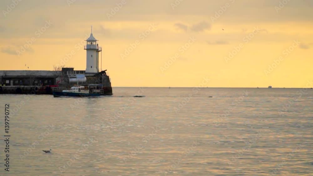 Pier with a lighthouse in the evening. The boat sails past. Slow motion,high speed camera Pier with a lighthouse in the evening. The boat sails past. Slow motion,high speed camera