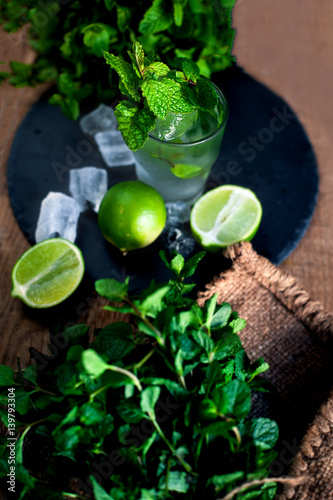 Fresh mojito drink with lime and mint in a glass on black stone board and wooden rustic table.