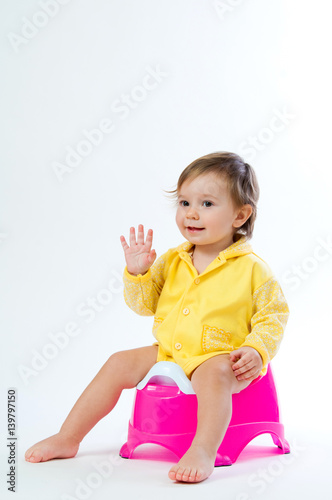 Little smiling girl sitting on a pot. Isolated on white background.