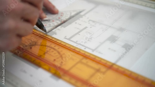 Architect drawing blueprints plan, graph, design, geometric shapes by pencil on large sheet of Tracing paper at office desk. Engineer hands, point of view POV Working with triangle ruler and pencil