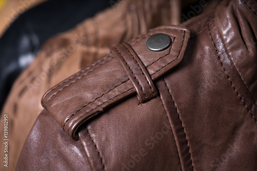 Brown leather jacket shoulder metal clasp button. Macro leather shoulder detail. Jacket on the rack