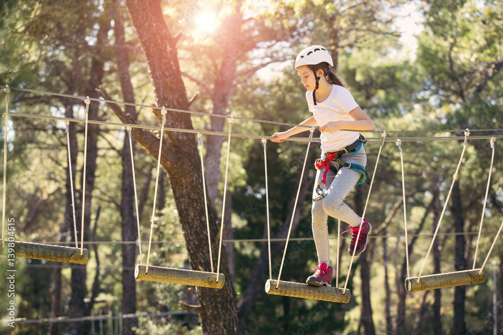 Happy school girl enjoying activity in a climbing adventure park on a summer day