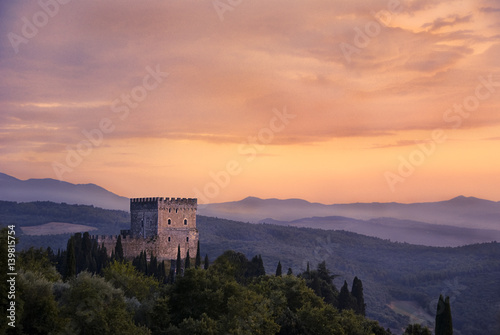 Castle at sunset in a hill in Val d'Orcia, Tuscany, surrounded by the wood in a misty and foggy sky.