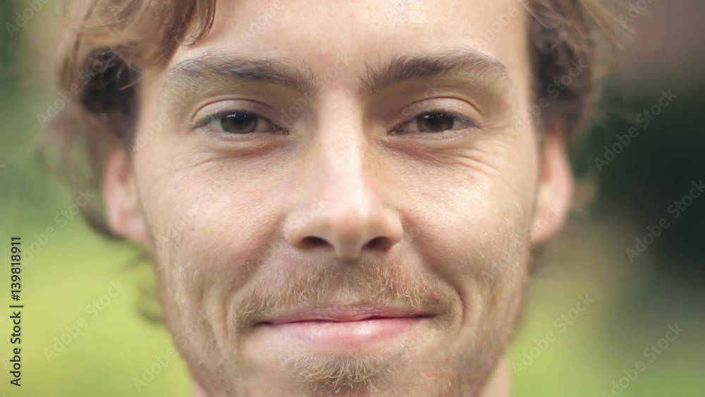 A young male steps up close to the camera and smiles directly, very shallow focus.