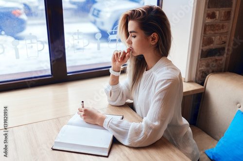 Young blond girl making notes in a notebook while sitting at the table