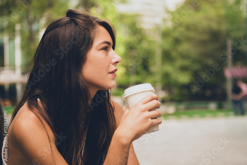 Side view of dreamy young woman having a cup of coffee outside. © progat