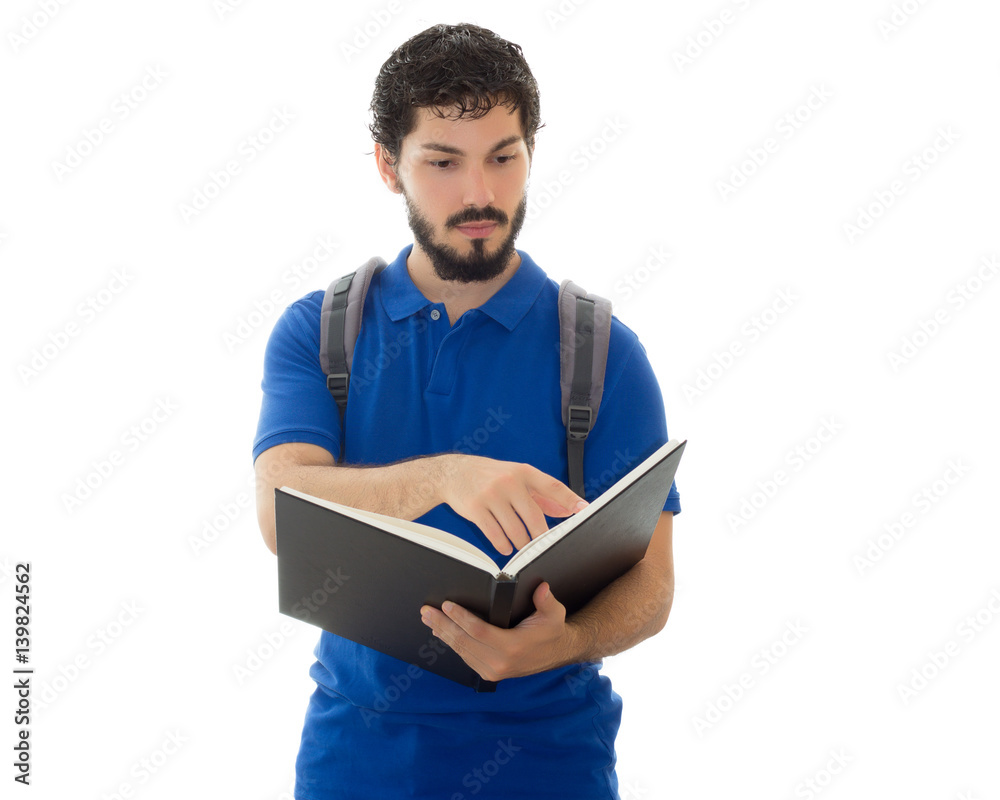 Young college student observes notes in his notebook with his backpack on his back. Young man wearing blue polo shirt, white background, copy space. Young college student observes notes in his notebook with his backpack on his back. Young man wearing blue polo shirt, white background, copy space.