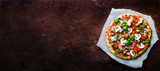 Fresh italian pizza with mushrooms, ham, tomatoes, cheese, olive, basil on backing paper, dark rustic background. Copy space. Homemade with love. Fast delivery. Recipe and menu. Banner.