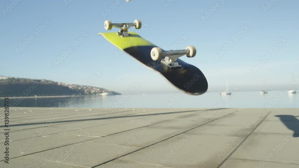 SLOW MOTION, CLOSE UP, DOF: Unrecognizable skateboarder skateboarding and jumping 360 flip trick on promenade along the ocean in sunny summer. Skateboarder riding skateboard jumping kickflip trick