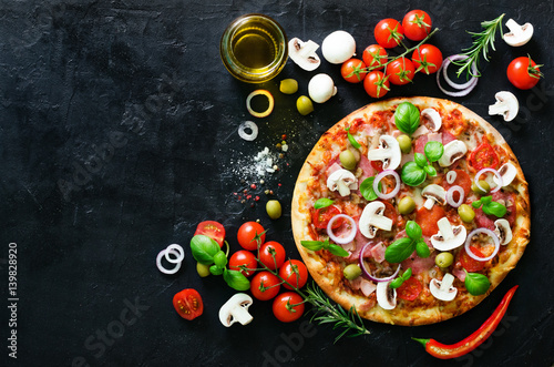 Food ingredients and spices for cooking mushrooms, tomatoes, cheese, onion, oil, pepper, salt, basil, olive and delicious italian pizza on black concrete background. Copyspace. Top view.