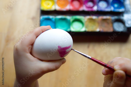 Child decorating easter egg with water colour