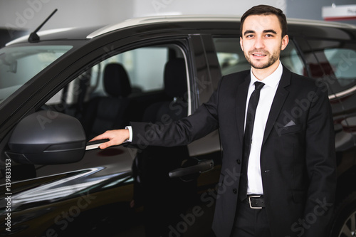Handsome young businessman in suit standing near car