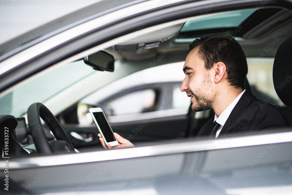 Businessman in car reading message or smth on smartphone