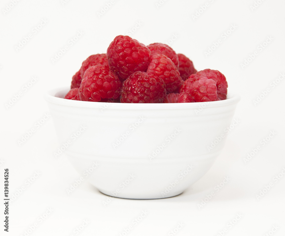 Red raspberries in a white bowl against a white background Red raspberries in a white bowl against a white background