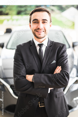 relaxed young businessman or salesman with hands crossed in front of car photo