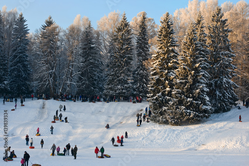 Sunny landscape. Park in a snowy day. Happy families. People play in snow together. Winter fun. Riding on inflatable sled. Sledding. Pavlovsk, Saint-Petersburg