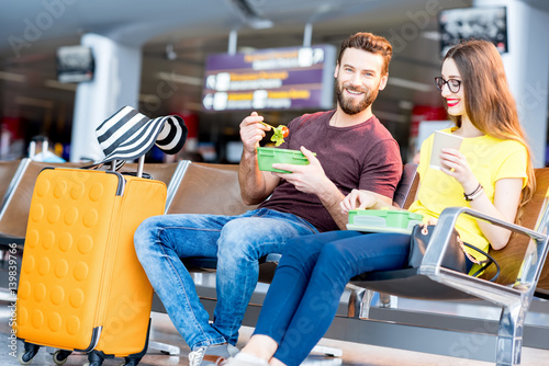 Young couple having a snack with lunch boxes at the waiting hall of the airport during their vacation