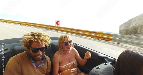 Young carefree people on summer holiday having fun driving in red convertible 