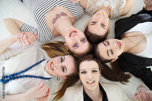A group of joyful elegant girls lies in a circle, a top view, on a white background.