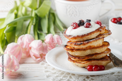 Breakfast. Fritters with sour cream and fresh berries. Pancakes. A Cup of tea, cranberries, black currant and flowers on the table. Selective focus