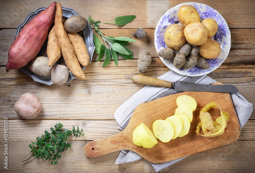 Five varieties of raw potatoes on rustic wooden table, top view.