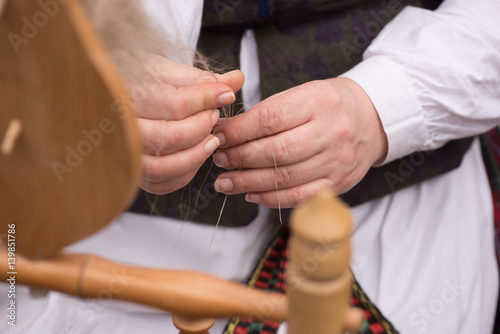 Hands of woman in action spinning wool into yarn with a spinning wheel 
