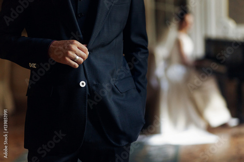 stylish handsome groom hand with silver ring on suit posing and elegant bride playing the fortepiano. unusual luxury wedding in retro style