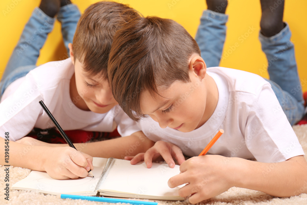 Twin brothers drawing in notebook on floor Twin brothers drawing in notebook on floor