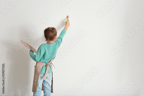 Cute little girl painting on light wall