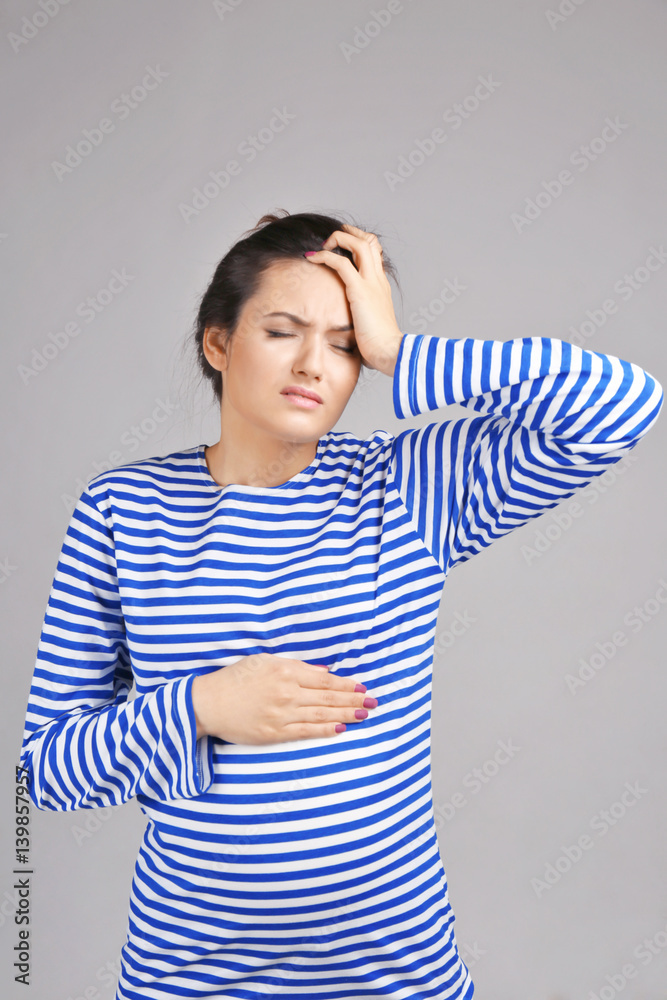 Young pregnant woman suffering from headache on grey background Young pregnant woman suffering from headache on grey background