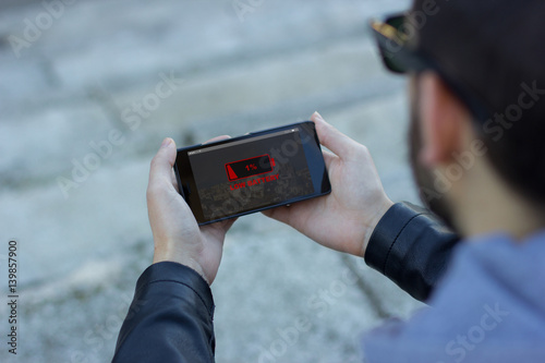 Man outdoors holding his smart phone with low battery alert message on the screen 
