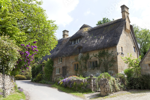 Thatched roof, stone cottage with flowering gardens,  by a country road, on a summer sunny day .