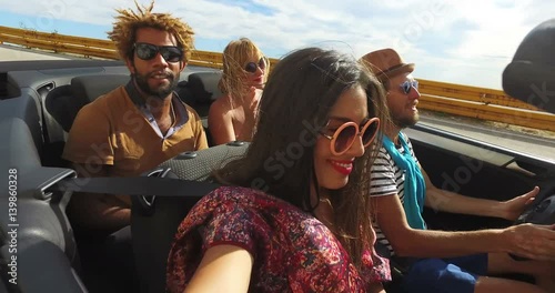 Attractive young people enjoying music while driving in convertible 