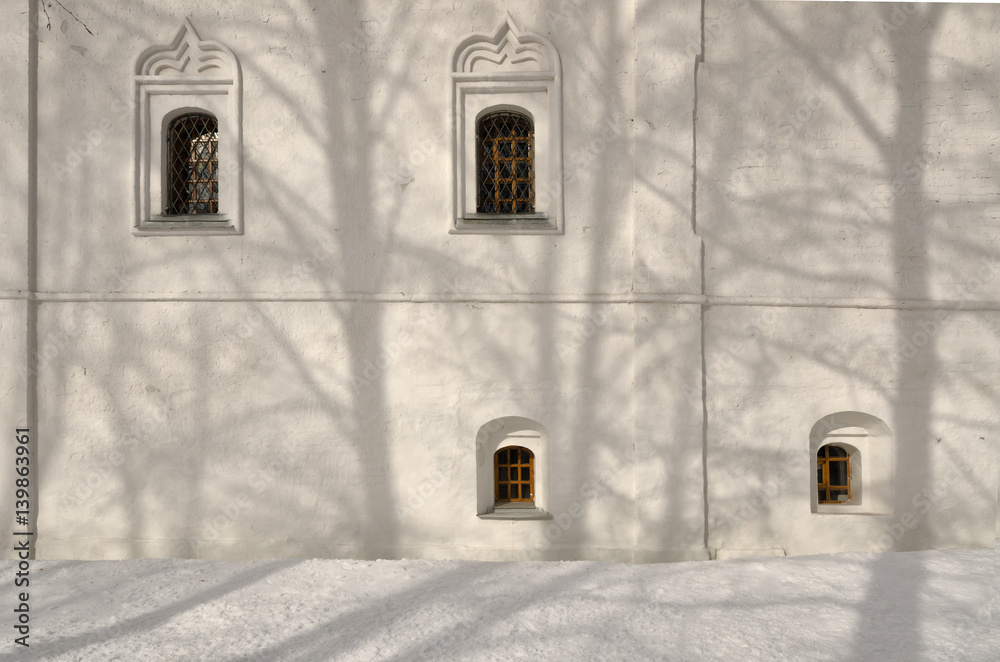 White wall of the Russian Orthodox Church with windows and shadows of trees. Winter. Daylight.