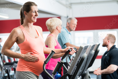 Schwangere Frau und Senioren trainieren am Crosstrainer im Fitnessstudio