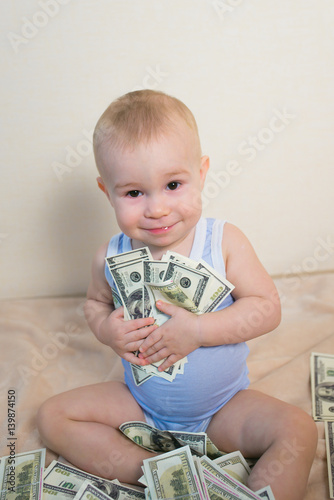 Happy baby boy playing with money, hugging hundreds of dollars photo