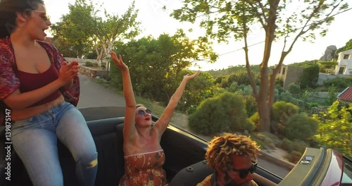 Beautiful young brunette sitting on hood of convertible and dancing to music 