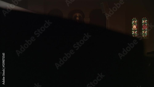 Woman kneeling in ray of sunlight in a Catholic church, viewed from across nave