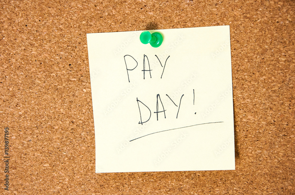 Paper note written with PAY DAY inscription on cork board Paper note written with PAY DAY inscription on cork board