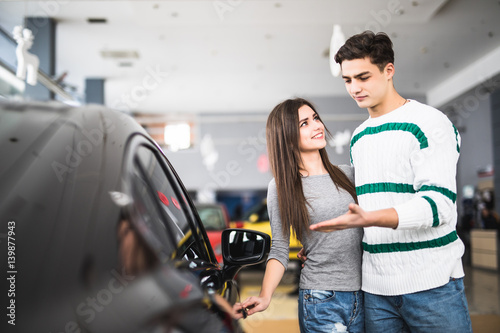 Beautiful young couple standing at the dealership choosing the car to buy photo