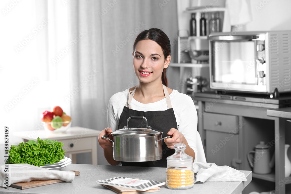 Young woman sitting at kitchen table and holding saucepan Young woman sitting at kitchen table and holding saucepan