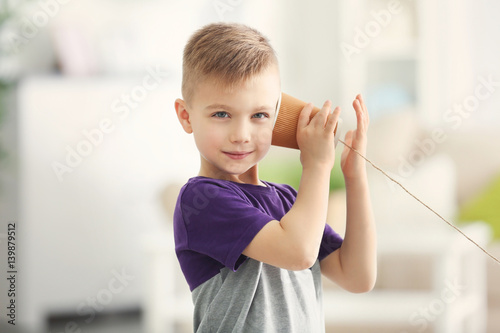 Cute little boy using plastic cup as telephone while playing at home photo